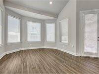 Large room with large bay windows, wood flooring, and a door leading to the back patio.