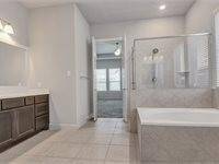 This bathroom features a spacious layout with a large bathtub, a glass-enclosed shower, and a dual-sink vanity with ample storage. The neutral tile flooring and soft lighting create a bright and inviting atmosphere.