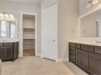 This bathroom features dual vanities with dark cabinetry, a large mirror, and neutral tile flooring. It includes a walk-in closet for ample storage and a bright, airy feel.