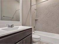 Bathroom 3 with a sleek vanity, a large mirror, a toilet, and a bathtub with a tiled shower area. The design is clean and contemporary.