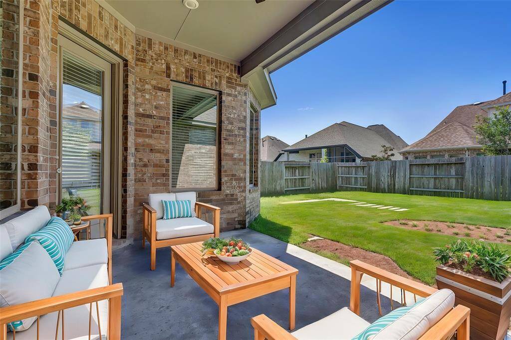 Covered patio with brick exterior walls, opening to a fenced backyard with a well-maintained lawn, ideal for outdoor activities.