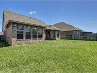 Backyard with a spacious lawn, fenced for privacy. The exterior features a covered patio area, ideal for outdoor activities.