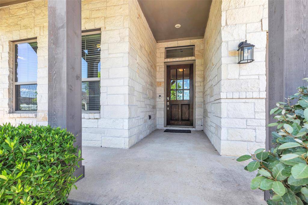 Welcoming front porch with a covered entryway, stone exterior, and a wooden door, accented by outdoor lighting and greenery.