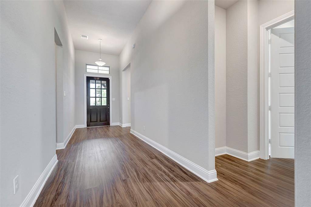Bright and spacious hallway with lightly tinted walls, dark wood flooring, and a stylish front door with glass panels, creating an inviting entryway.