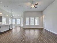 Spacious, open-concept living area with wood flooring, high ceilings, and ample natural light. The room features a modern kitchen with an island and pendant lighting, offering a seamless flow for entertaining.