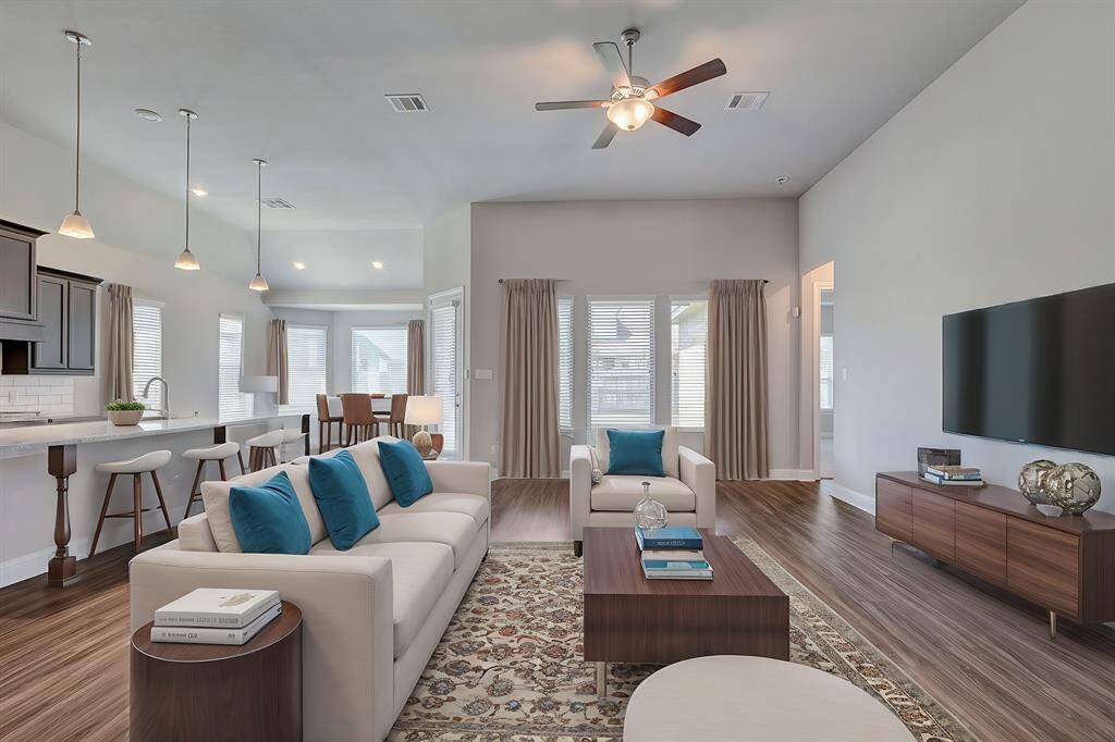 This modern open-concept living area features a spacious layout with a cozy seating arrangement, hardwood floors, and abundant natural light. The kitchen includes a large island with bar seating, pendant lighting, and sleek cabinetry, seamlessly flowing into the dining and living spaces. (Virtually staged)