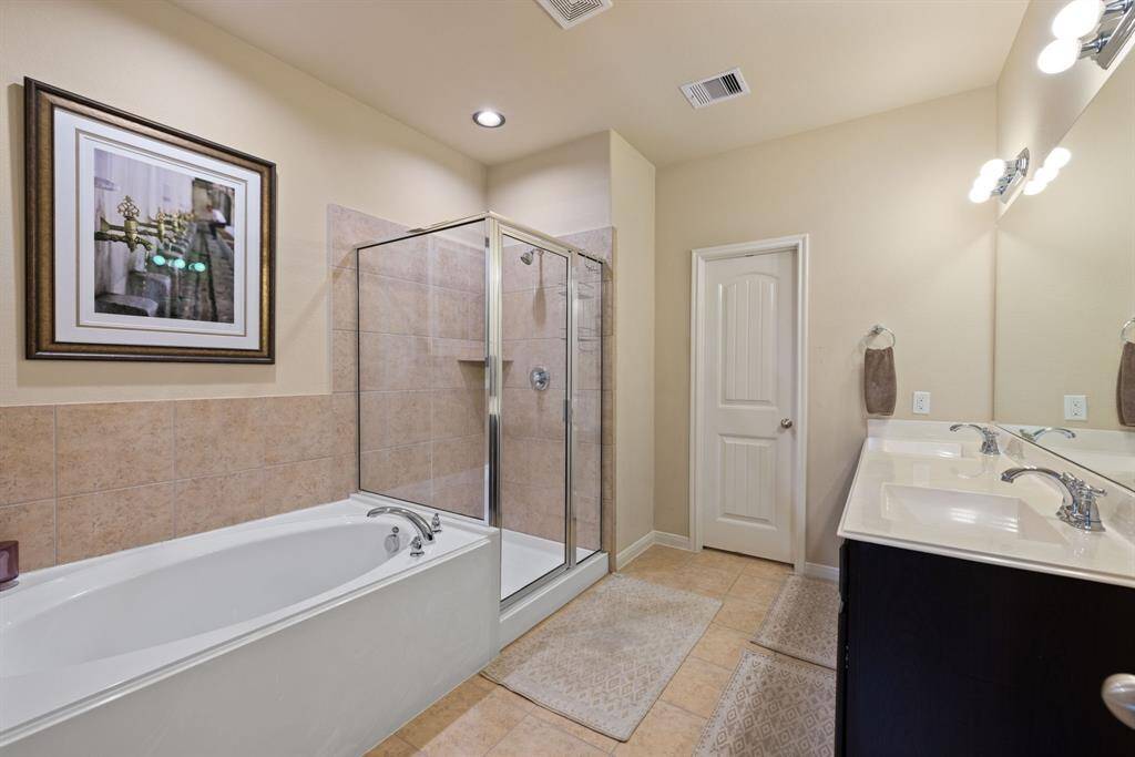 The primary bathroom offers a soaking bathtub and separate shower and dual vanity sinks. The neutral tile surround adds a touch of elegance, creating a calming and classic atmosphere.