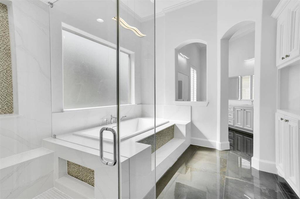 This primary bathroom is definitely move-in ready! Featuring an oversized walk-in shower, lots of white cabinets for storage, light countertops, spacious walk-in closet with shelving, high ceilings, neutral paint, jetted tub with glass window allowing natural light to brighten up the whole area, sleek and modern finishes.