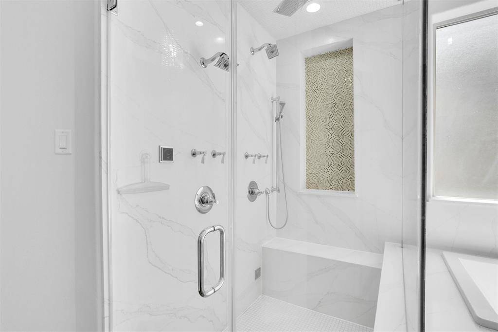 This additional view of the primary bathroom showcases the walk in shower with modern finishes and extra space for seating.