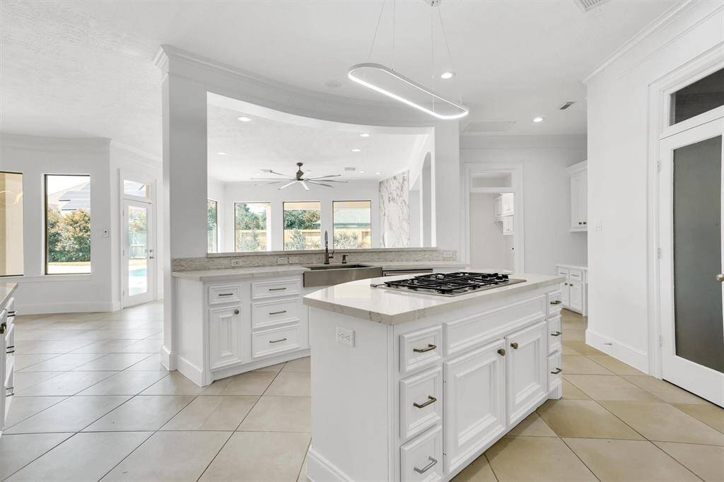 This stunning kitchen displays such beautiful white cabinets, neutral paint, light modern backsplash, and stainless steel appliances, oversized kitchen island with extra storage, breakfast bar, recessed lighting and cooktop.