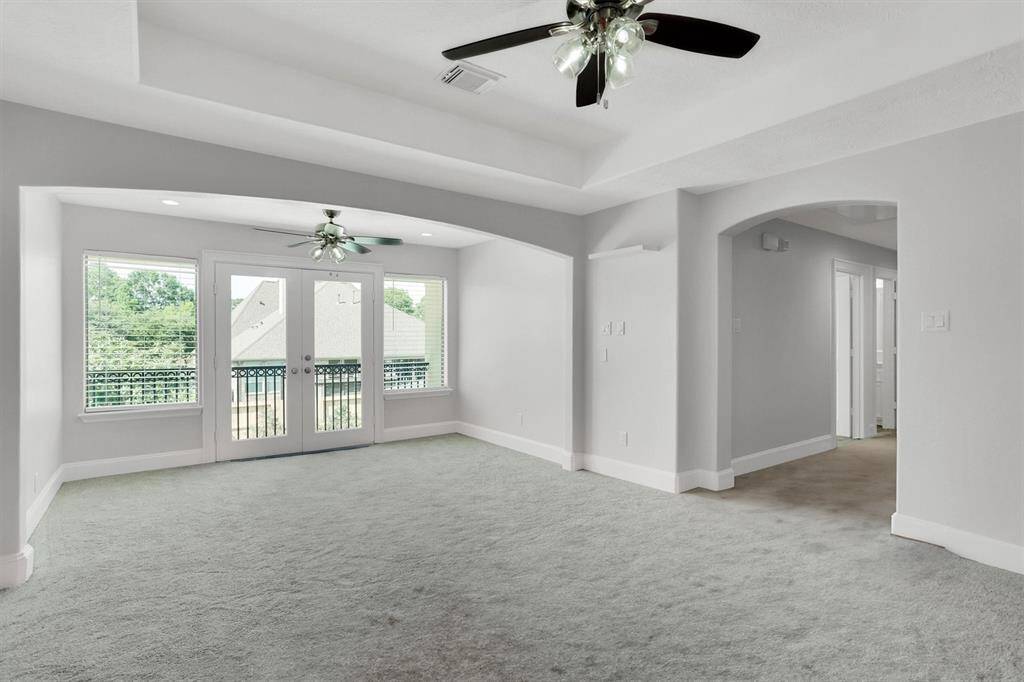 Anther view of the game room with plenty of space for extra seating, featuring large windows, ceiling fans, carpet flooring, and an arched way that leads to the secondary bedrooms.