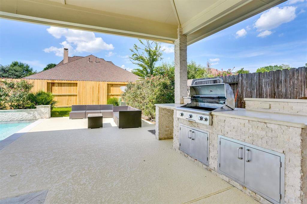 Well-designed outdoor area that includes a built-in grill station on a covered patio. The grill is set into a light-colored stone countertop with stainless steel cabinets beneath it.