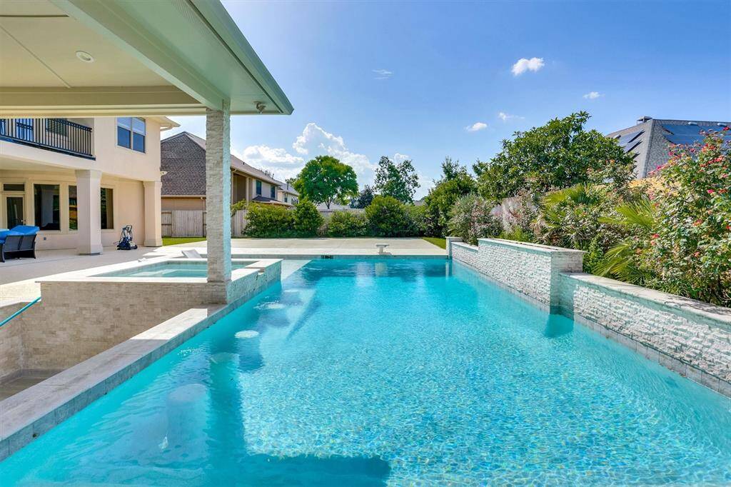 Comfortable outdoor seating is arranged near the pool, and the area is well-landscaped with bushes and plants along the fence line, providing privacy and a pleasant atmosphere. The overall setting is perfect for relaxation and outdoor gatherings.