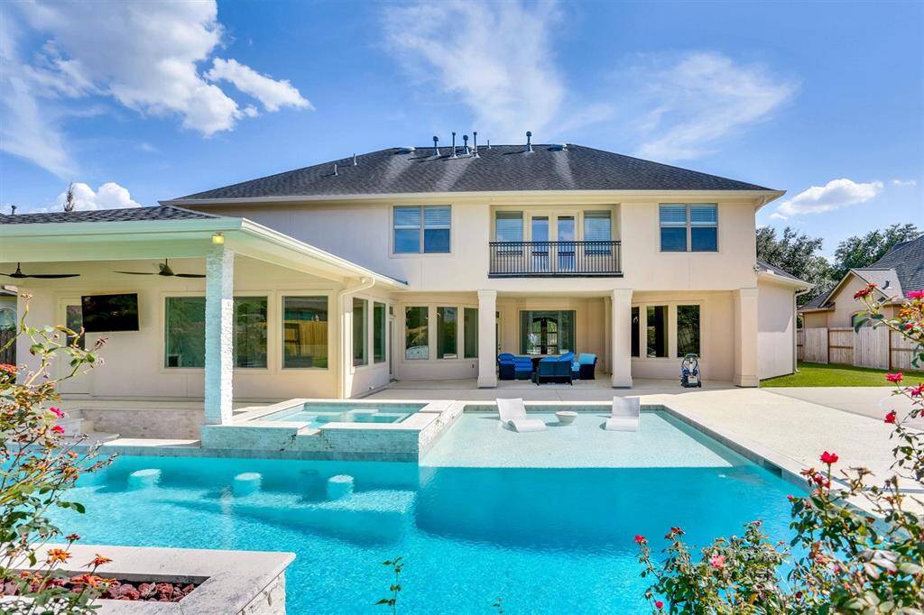 Luxurious and well-maintained property designed for comfort and outdoor entertainment. Beautiful outdoor space featuring a pool and a covered patio. The pool has a modern design with clean lines and a light-colored stone surround. The patio area is spacious, equipped with a built-in grill and countertop for outdoor cooking. There are ceiling fans installed for comfort, and a mounted TV.