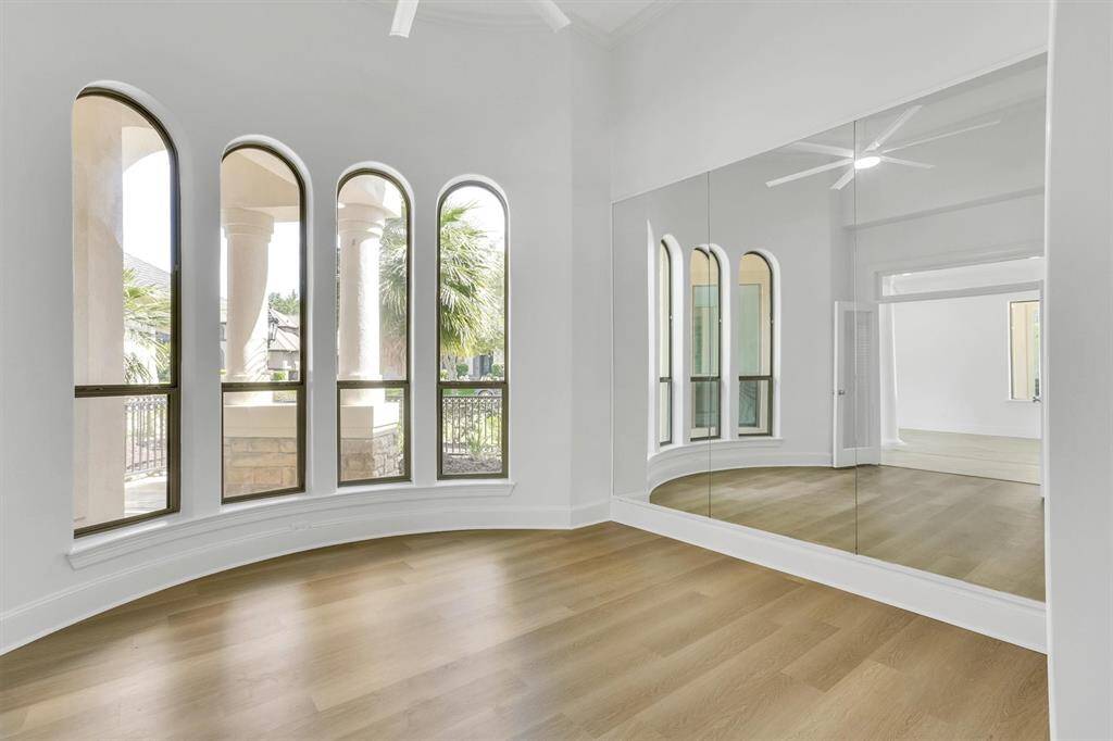 Another view of the home office/study room featuring large arched glass windows, large mirror, and beautiful fwood floors.