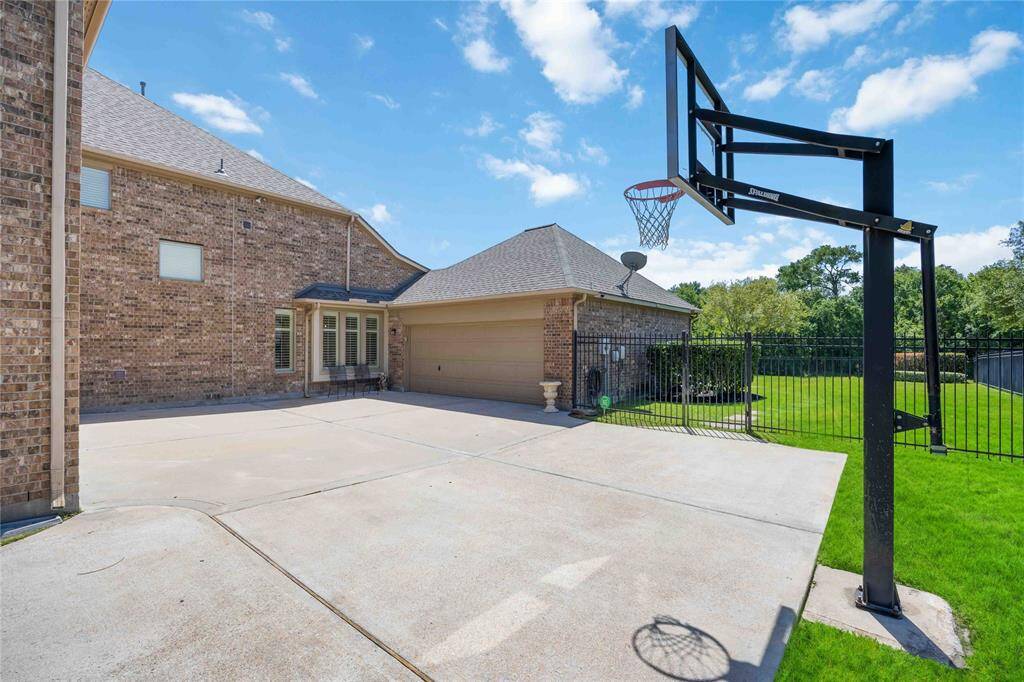 Side driveway featuring a basketball court and wrought iron fence.