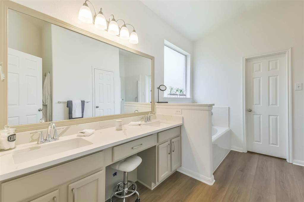 A luxurious primary bathroom showcases sleek new quartz countertops, new cabinets, a framed mirror, and new lighting.
