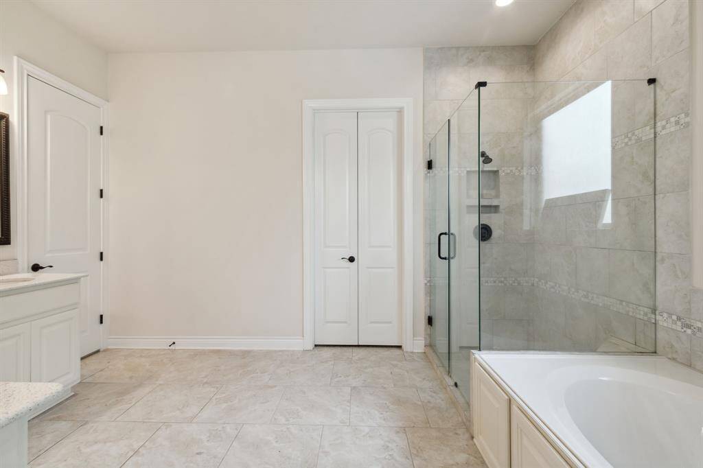 Primary ensuite with soaking tub and frameless clear glass shower with black accents.