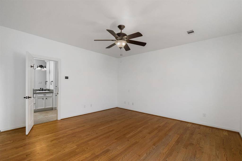 Primary bedroom with wood floors, ceiling fan and en suite bath. Window in bedroom overlooks pool and backyard