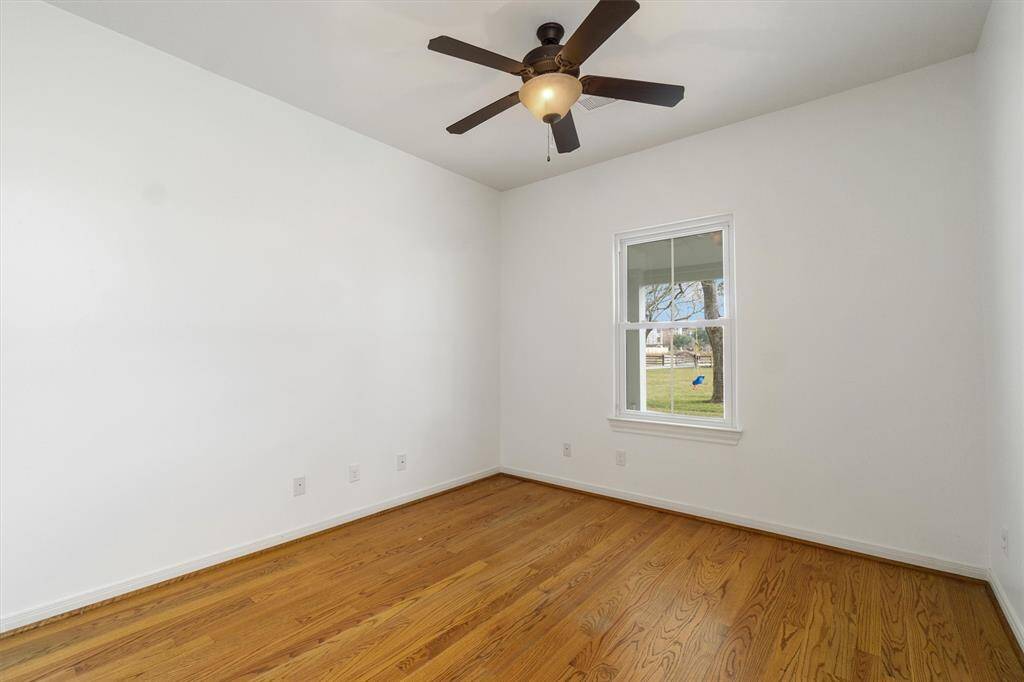 Secondary bedroom downstairs with wood floors, ceiling fan and window overlooking the front yard.