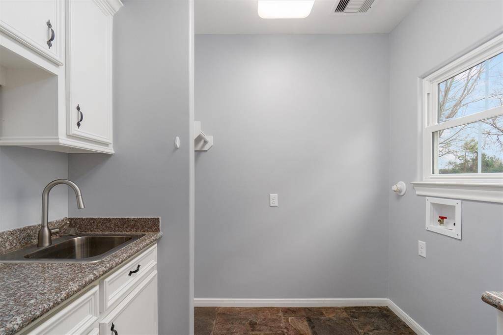 Laundry room accented with pocket door, sink, counter space and storage for essentials. Natural slate flooring.