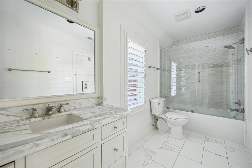 This en suite bath showcases refined finishes including a marble-topped vanity, frameless glass tub/shower, and crisp tile flooring—creating a clean, timeless retreat.