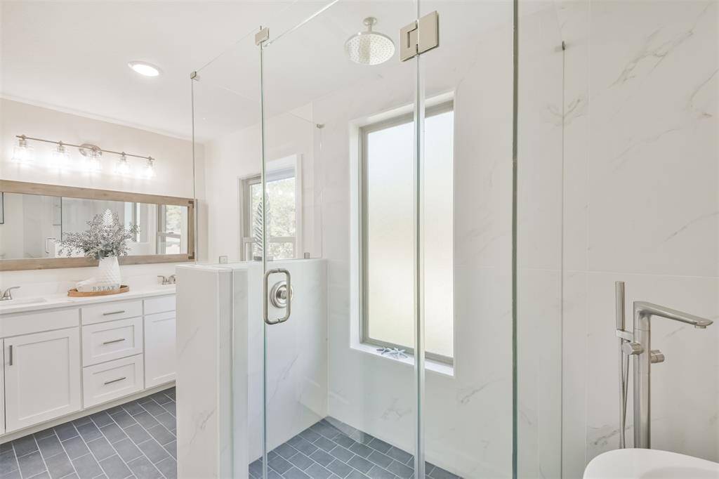 Primary bathroom has new step in shower with frameless glass, rain shower head and beautiful new tile flooring.