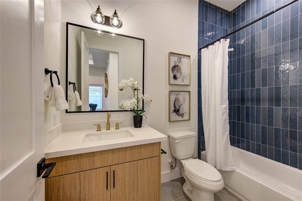 Bathroom 2 features designer tilework, European style white oak colored cabinetry, white quartz counters, and champagne bronze delta shower fixtures.