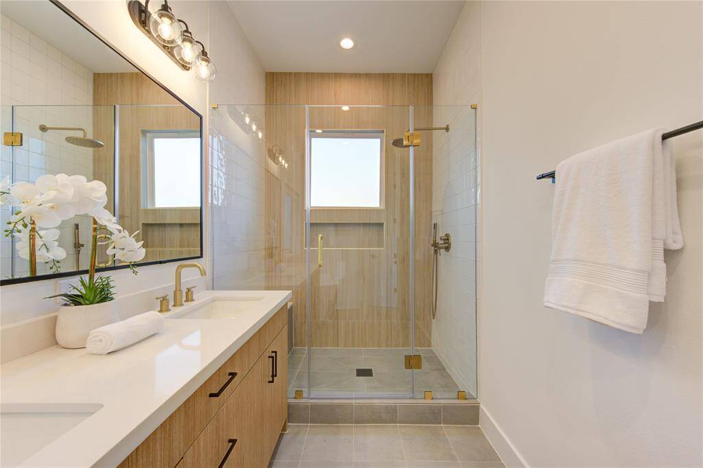 Primary bathroom with large shower and soaking tub. Bathroom features designer tilework, European style white oak colored cabinetry, white quartz counters, and champagne bronze delta shower fixtures.