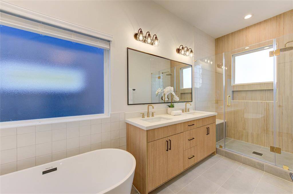 Primary bathroom with large shower and soaking tub. Bathroom features designer tilework, European style white oak colored cabinetry, white quartz counters, and champagne bronze delta shower fixtures.