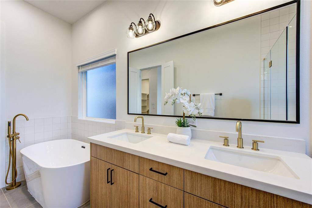 Primary bathroom with large shower and soaking tub. Bathroom features designer tilework, European style white oak colored cabinetry, white quartz counters, and champagne bronze delta shower fixtures.