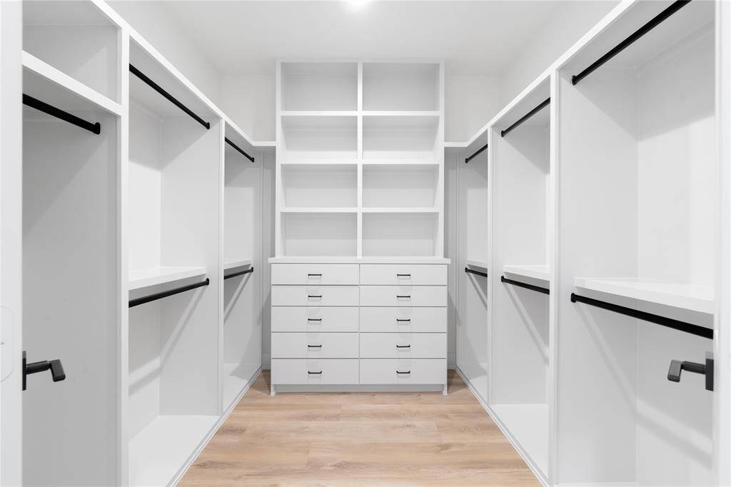 A luxurious walk-in primary closet, designed for maximum organization and style. This expansive space offers a blend of custom-built storage solutions and a sleek, modern design to keep everything effortlessly organized.