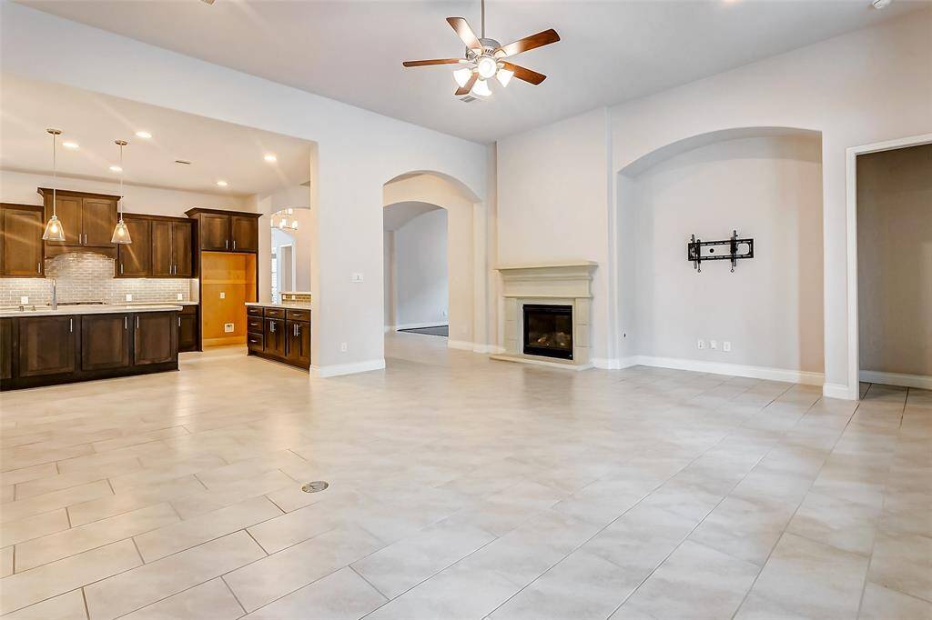 A soaring ceiling with a fan adds to the airy feel, while a dedicated nook for an entertainment center, complete with a TV mount, ensures the room is perfectly set up for media enjoyment. Nearby, a cozy gas-log fireplace provides a touch of warmth and romance, making the space even more inviting.