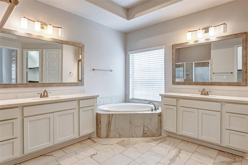 The spa-like bathroom offers a serene space designed for ultimate relaxation & indulgence. Featuring a high tray ceiling that adds an element of grandeur, gleaming tile floors that reflect light, & a large window with 2-inch blinds that allow natural light to fill the space when desired, this bathroom is both beautiful & functional.