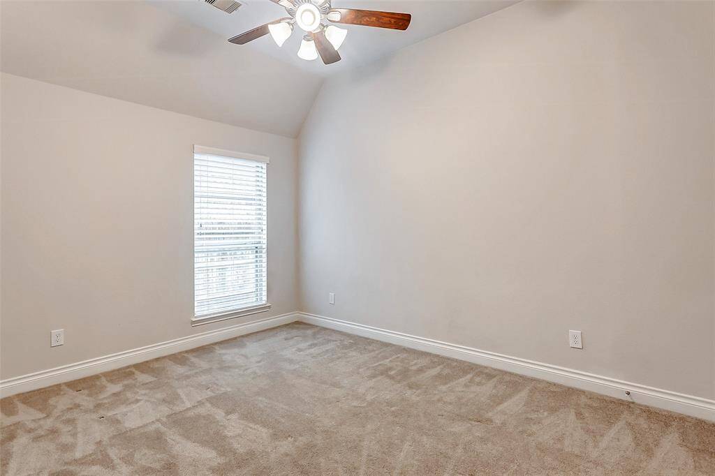 This secondary bedroom boasts a high ceiling with a ceiling fan, enhancing the sense of space and comfort. Plush carpeting adds warmth and softness underfoot, while a large window, fitted with 2-inch blinds, allows natural light to flood the room, creating a bright and inviting atmosphere.