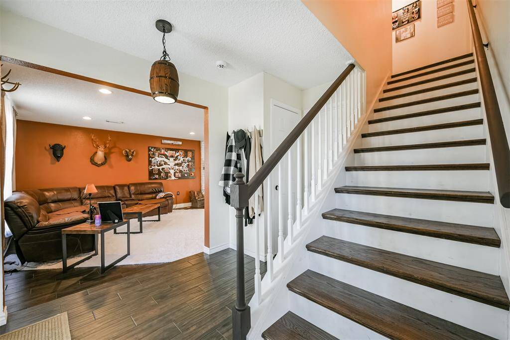 The photo shows a cozy entryway with a staircase leading upstairs and a living area with a warm, terracotta accent wall, The space offers a welcoming atmosphere.