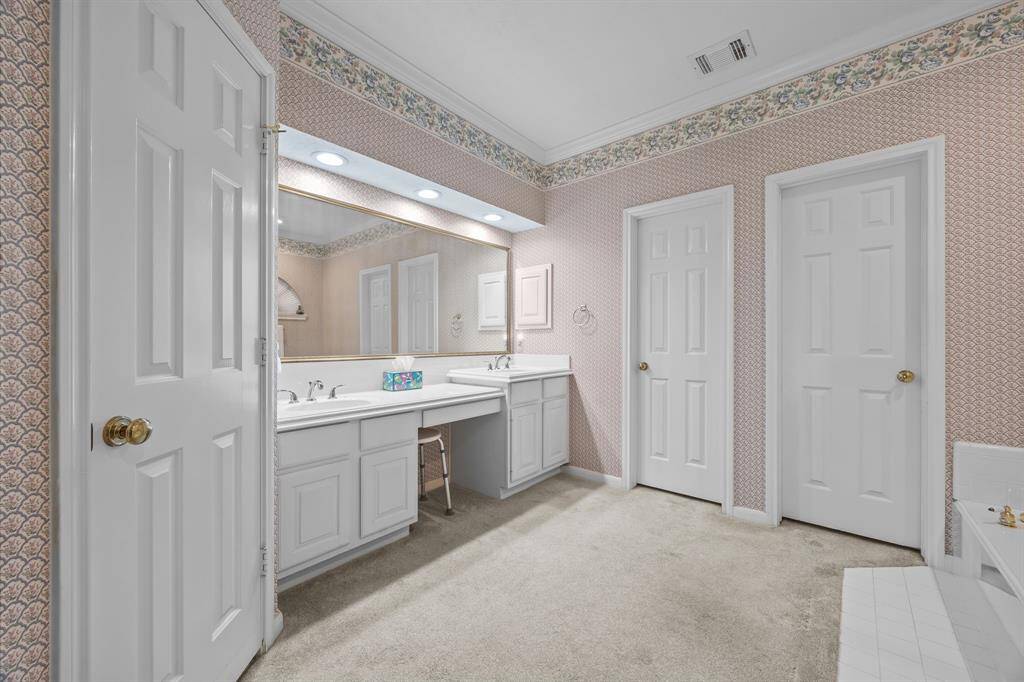 Spacious primary bathroom featuring double sinks, a vanity area, and two walk-in closets for ample storage.
