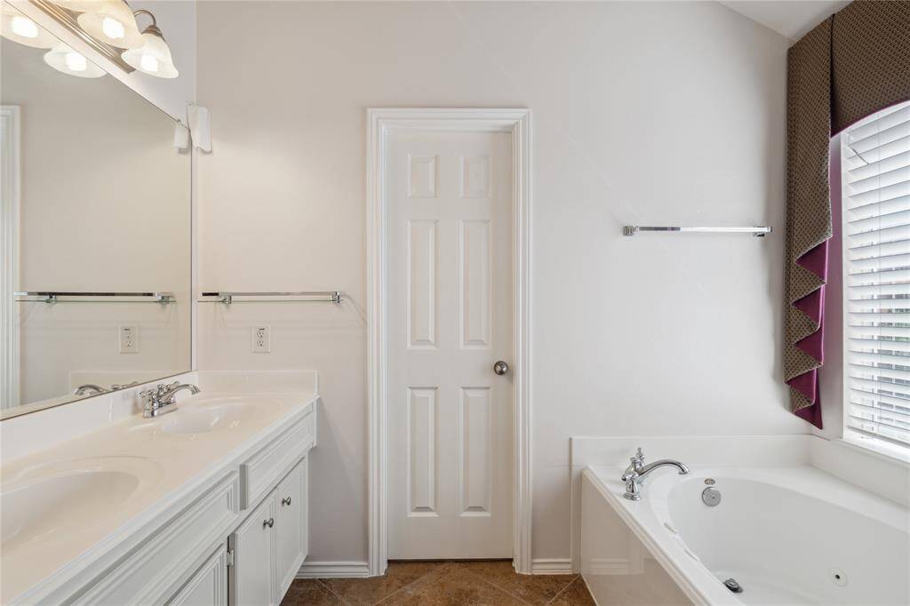 Another view of the primary bath showcases the soaking tub set beneath a large window with blinds—inviting natural light while maintaining privacy.