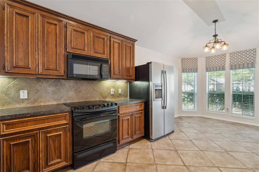The kitchen features large tile flooring that extends into a bright breakfast area, where three generously sized windows overlook the front yard and fill the space with warm natural light.