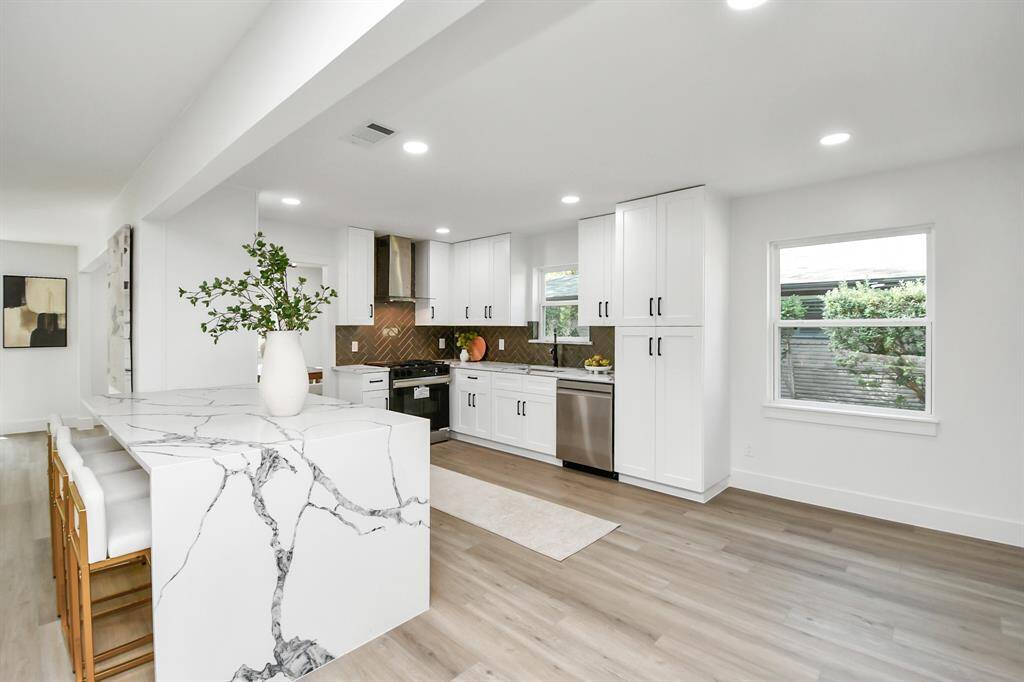 Modern kitchen featuring solid wood cabinets with soft close drawers and doors, quartz countertops, stainless steel appliances, and a central island with seating space. Natural light from large windows complements the bright, open-plan design.