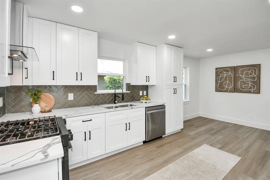 This photo showcases a modern kitchen with solid wood cabinets with soft close drawers and door, stainless steel appliances, herringbone tile backsplash, and ample natural light. It features a gas range and a sleek, minimalist design.