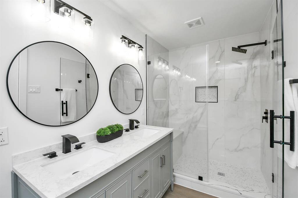 Modern bathroom featuring a double vanity, under mount sink, two circular mirrors, sleek black fixtures, and a spacious walk-in shower with glass enclosure.