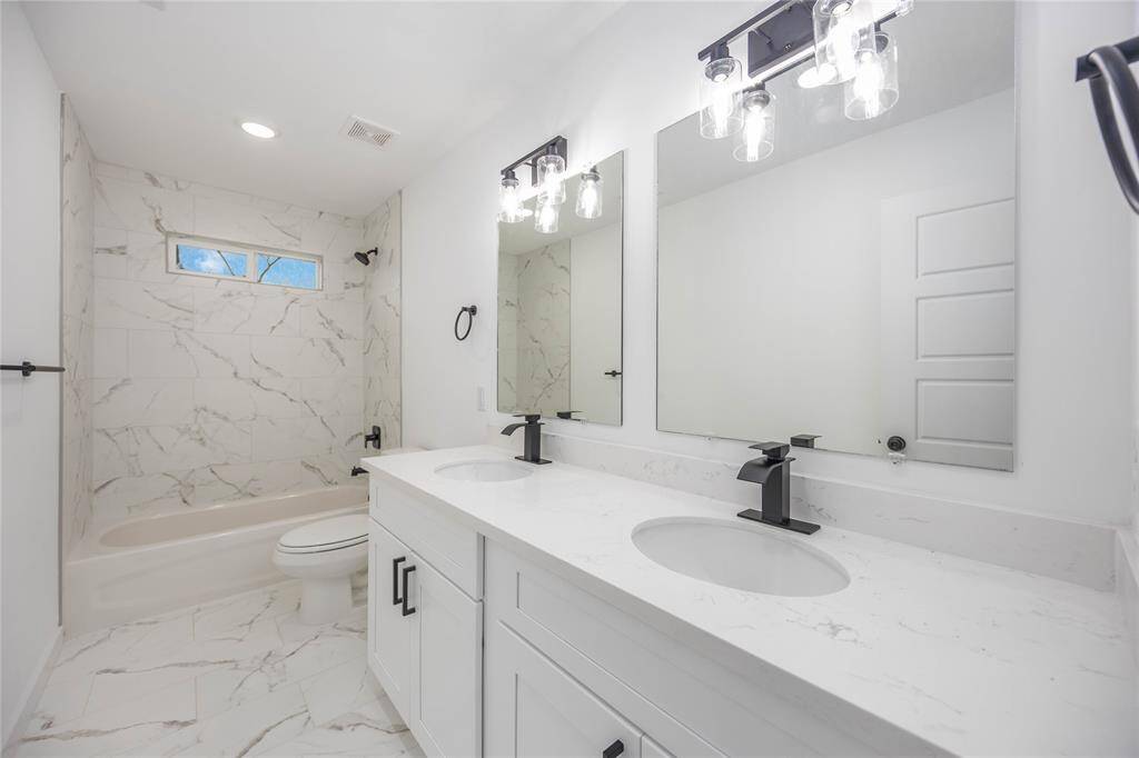 This stylish secondary bathroom features elegant marble tile flooring and a matching shower surround for a luxurious feel. The modern vanity with a quartz countertop, matte black fixtures, and ample lighting adds sophistication and functionality.