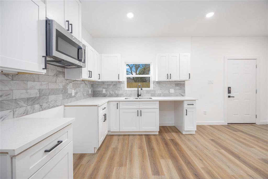 This modern kitchen boasts sleek white cabinetry, elegant marble backsplash, and stainless steel appliances for a polished look. The open layout, ample counter space, and natural light make it perfect for cooking and entertaining.