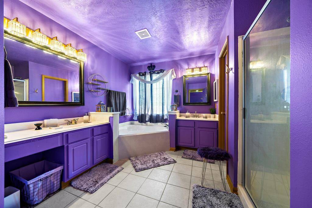 Primary bathroom featuring dual vanities with ample cabinet storage, a soaking tub, and a separate enclosed shower