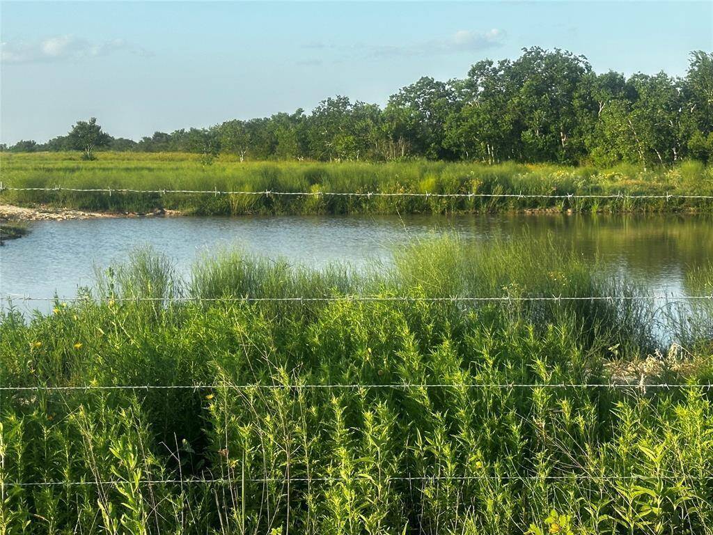 Scenic view of the pond near the front of the property, bordered by mature greenery and secured by a barbed wire fence—ideal for livestock and enhancing the peaceful setting.
