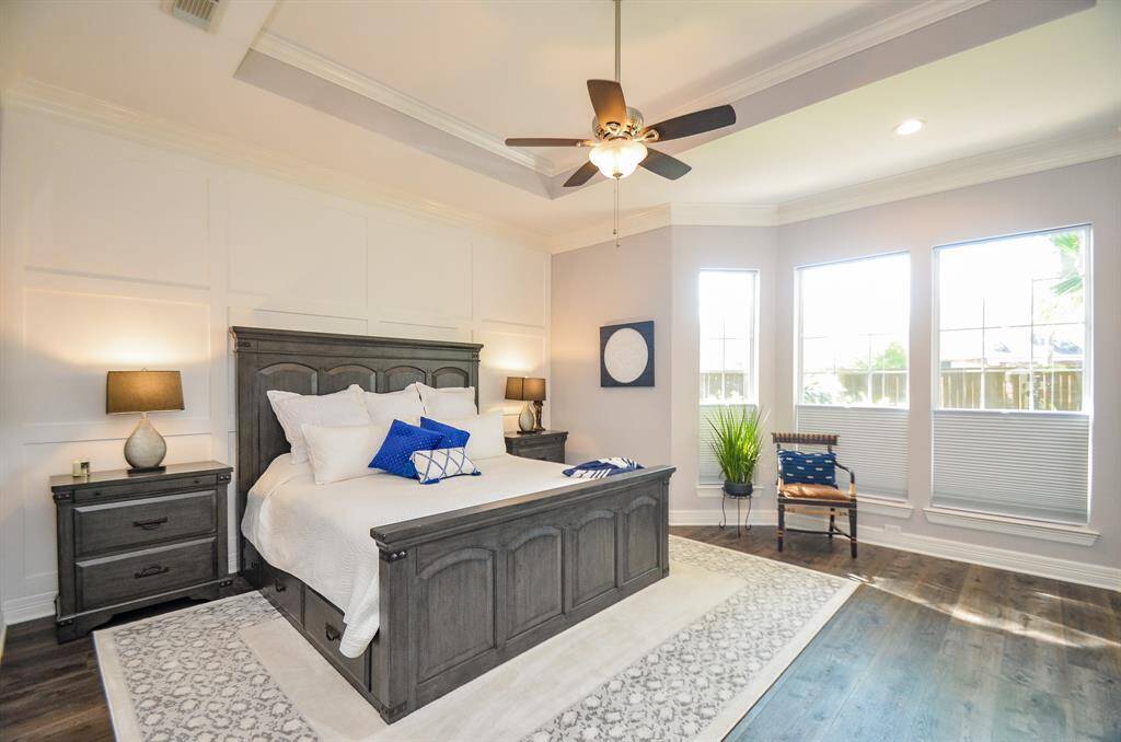 Pristine primary bedroom with a custom dimensional accent wall and sitting area with views of the walking path.