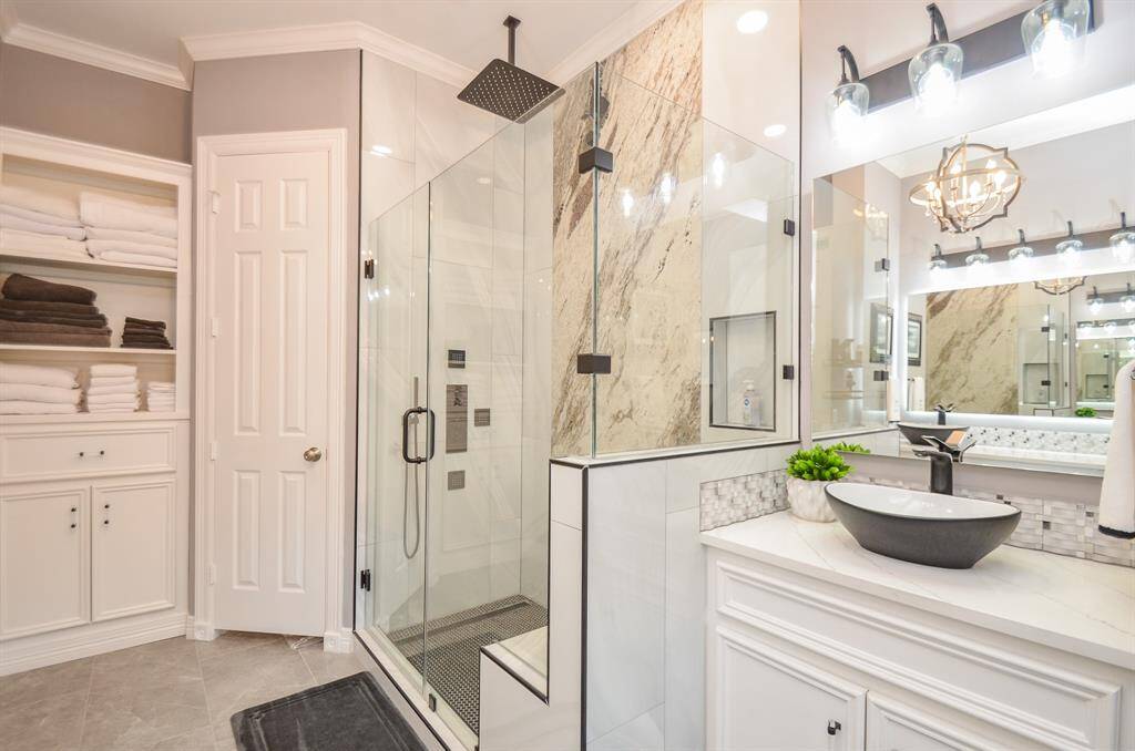 Second vanity and custom shower with frameless glass, built-in seat, rain showerhead, body sprays, and handheld sprayer. Check out the granite slab accent wall!