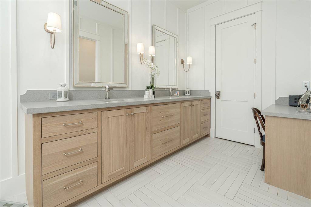The primary bathroom has a clean, neutral palette with white panel walls and a herringbone-patterned tile floor.