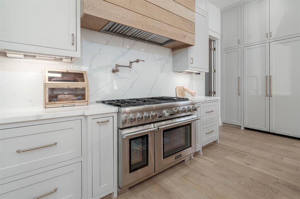 This modern kitchen features sleek white cabinetry, a stainless steel gas range with double ovens,
